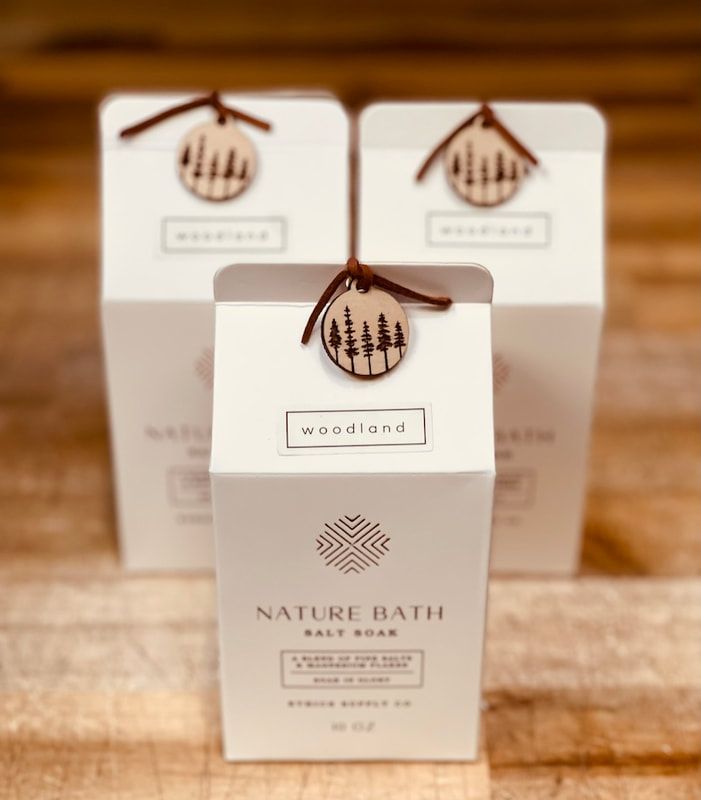 Three white Nature Bath soap boxes with brown tags on a wooden surface