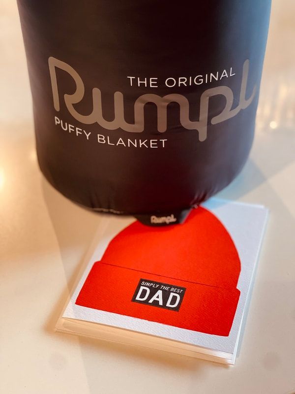 Red knit “DAD” beanie on a boxed stack beside a black Pumpy blanket package