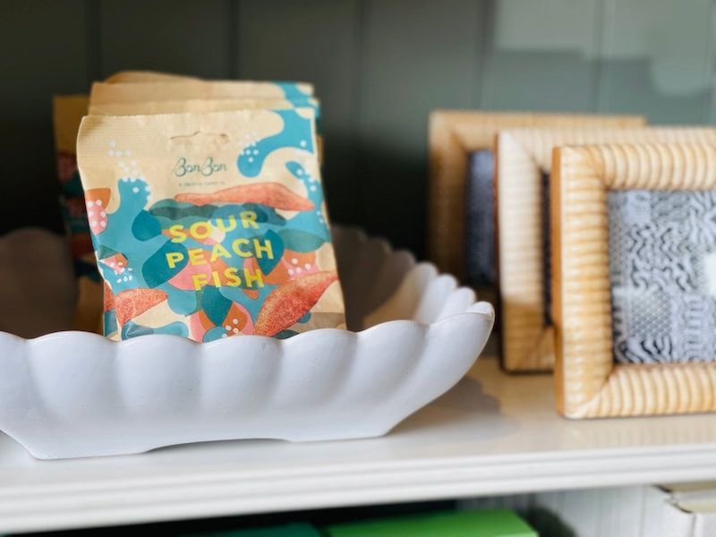 Bag of Sour Peach Fish candy on a white shell-shaped dish with woven frames in the background