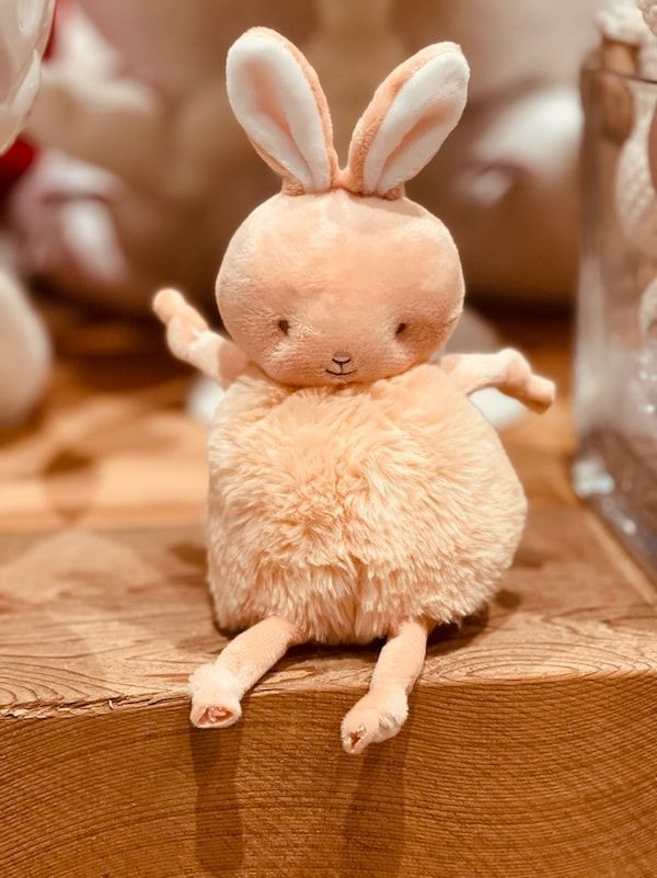 Small plush bunny with pink ears sitting on a wooden ledge, with legs dangling.