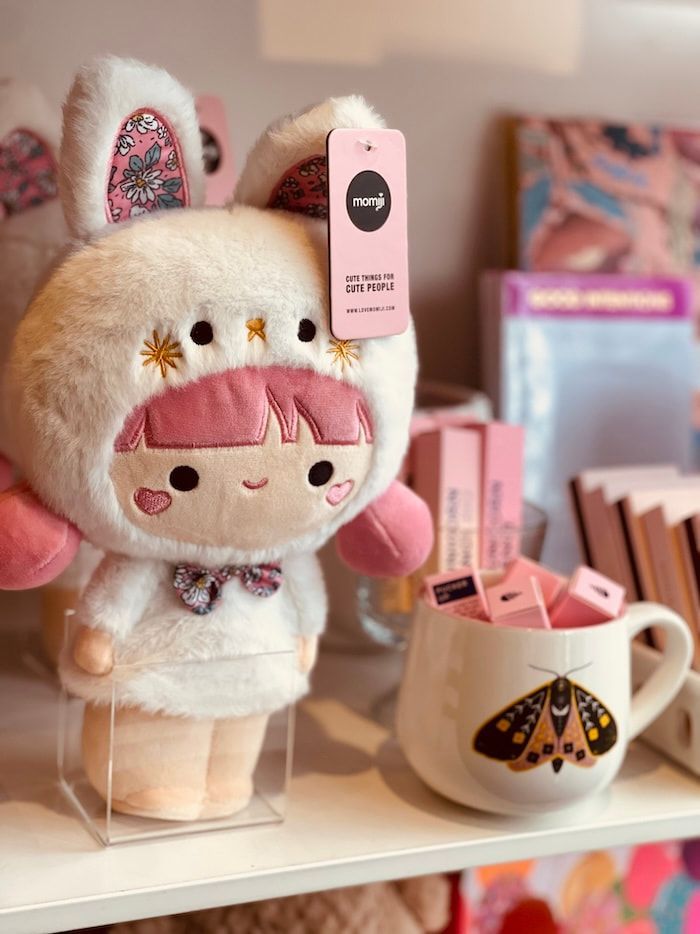 Plush bunny doll beside pink cosmetics on a shelf, with a white mug in a cozy display.