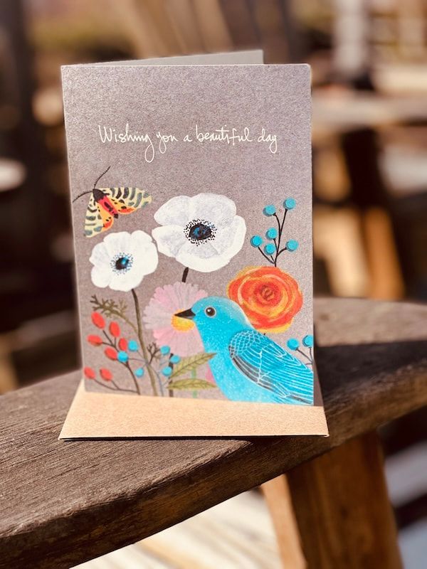 Handmade greeting card with blue bird, white flowers, and orange rose on a brown table