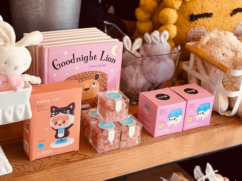 Pastel display of bunny plushes and pink cat-themed treat boxes on a wooden shelf