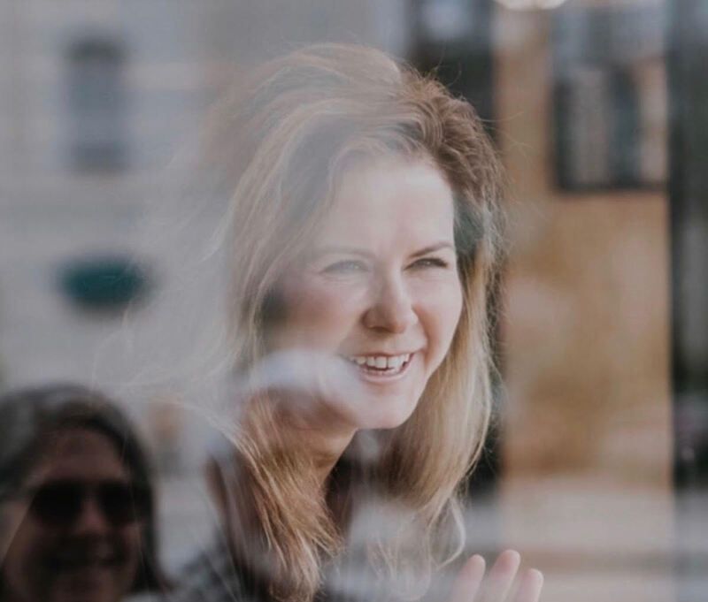 Smiling woman seen through a window reflection, with soft indoor light.