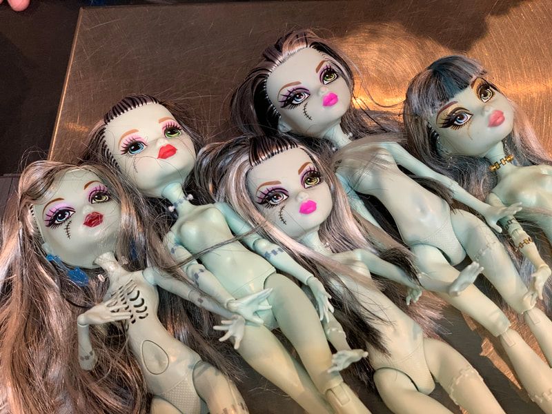 Five dolls with painted faces and pale bodies lying together on a brown surface