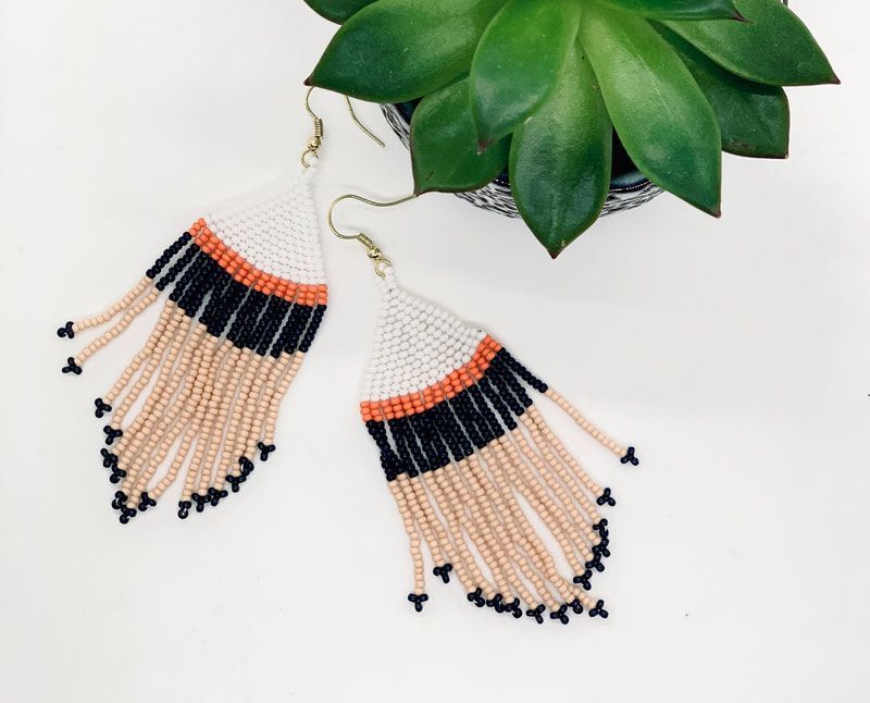 Beaded fringe earrings in peach, black, and white with green leaves above them on a white background