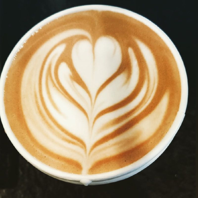 Top-down view of a latte with white heart-shaped foam art in a brown coffee cup