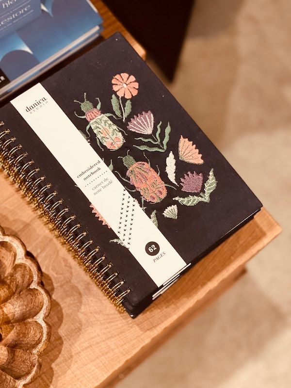 Notebook with floral cover on a wooden table beside a blue box and beige floor