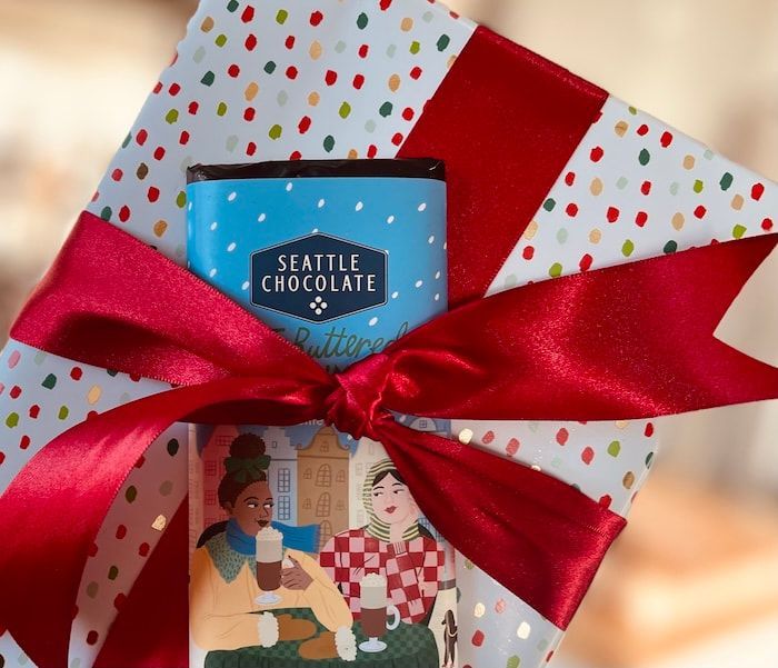 Gift bag with colorful polka-dot wrapping, a red ribbon bow, and a Seattle Chocolate bar.