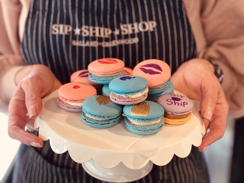 Hands holding a plate of pastel macarons with a birthday-style topper and striped apron in the background