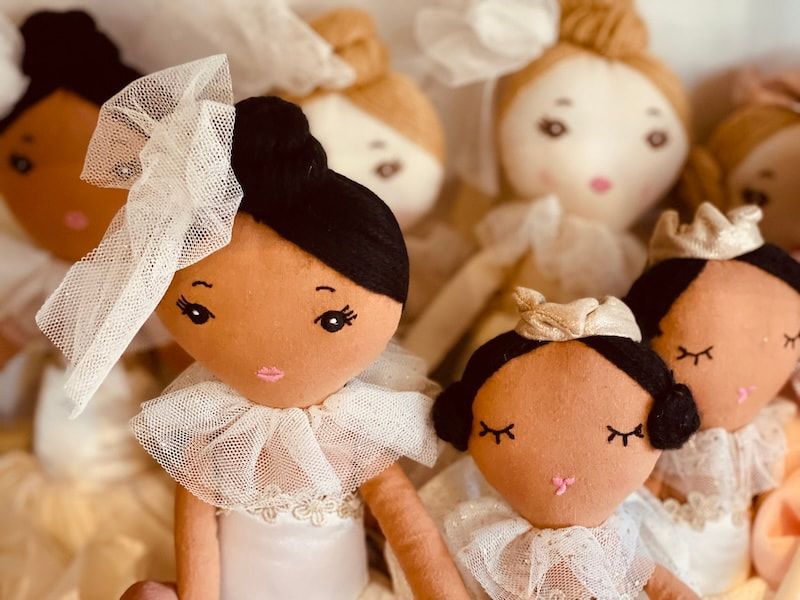 Small handmade cloth dolls with white tulle collars and bows, arranged in a soft, warm-toned group.