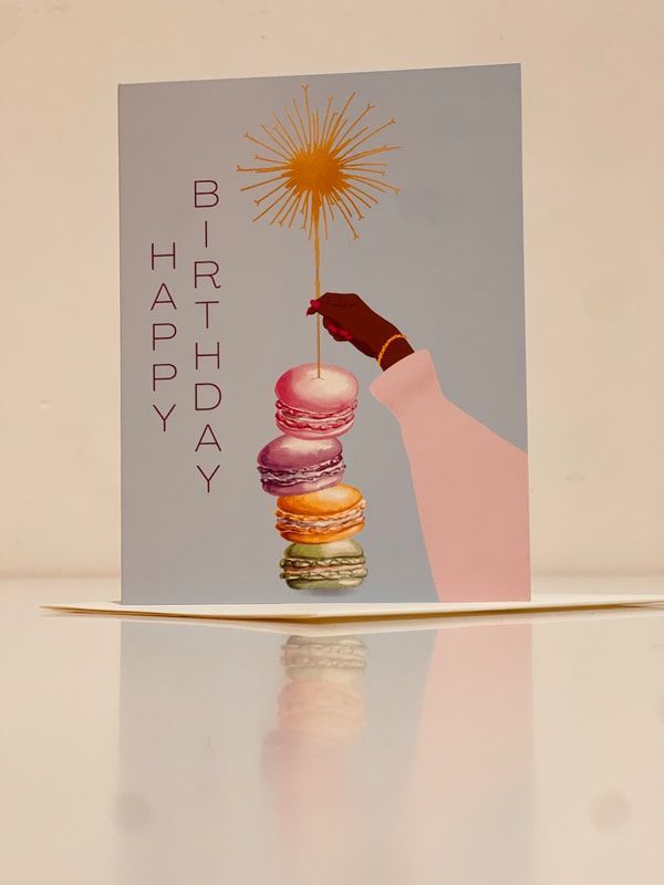 Birthday card with a hand stacking macarons and a lit sparkler, reading “Happy Birthday.”