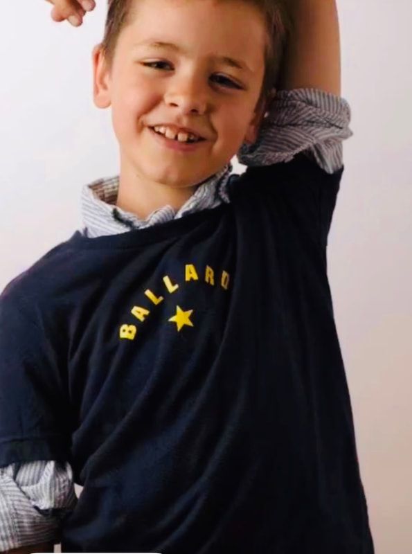 Smiling child in a navy shirt with a yellow star logo, stretching with one arm raised