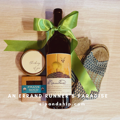 Gift basket with wine, snacks, and a green ribbon on a wooden surface, with “An Errand Runner’s Paradise” text