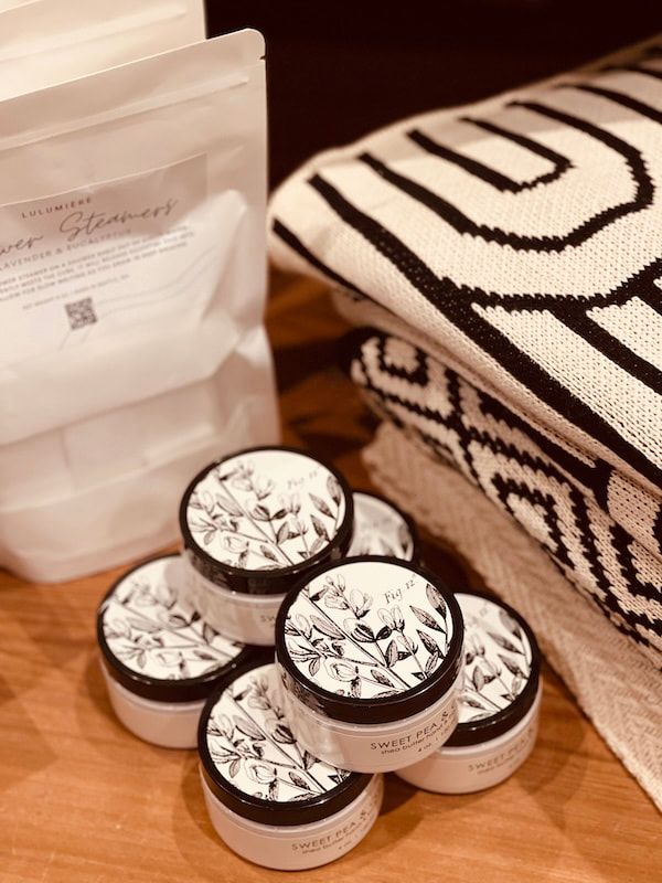 White pouches and four small round tins on a wooden table beside a black-and-white patterned towel