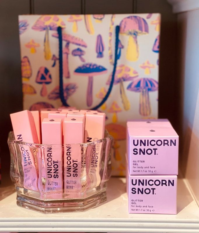 Unicorn Snot lip gloss display with pink tubes and box beside a colorful unicorn-themed sign