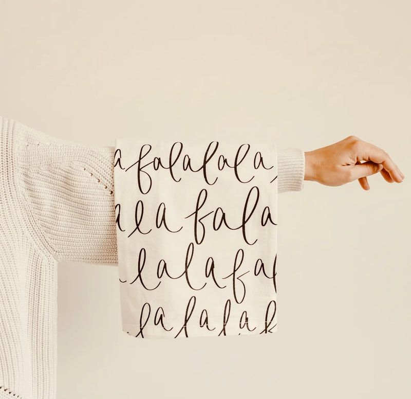 Arm in cream sweater showing white fabric with black handwritten “fa la la” pattern