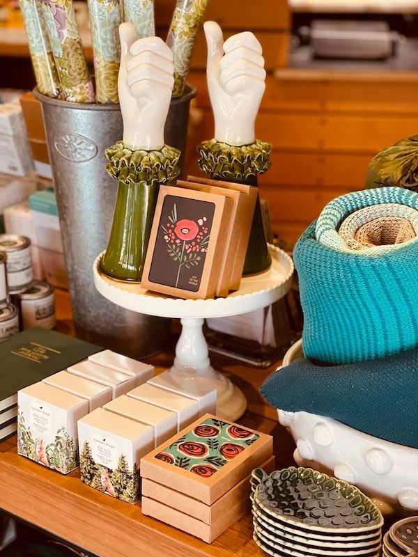 Display of candles, soaps, and decorative home goods on a white pedestal and wooden table