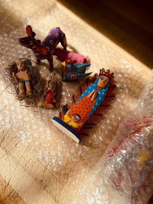 Small handmade dolls and colorful figurines resting on bubble wrap in a box.