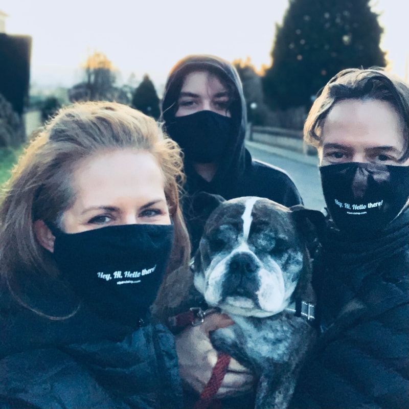 Three people in black masks posing with a black-and-white dog outdoors at dusk