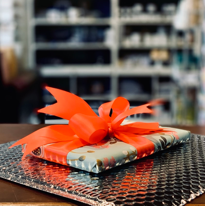 Gift-wrapped present with bright orange ribbon on a table, with blurred shelves in the background