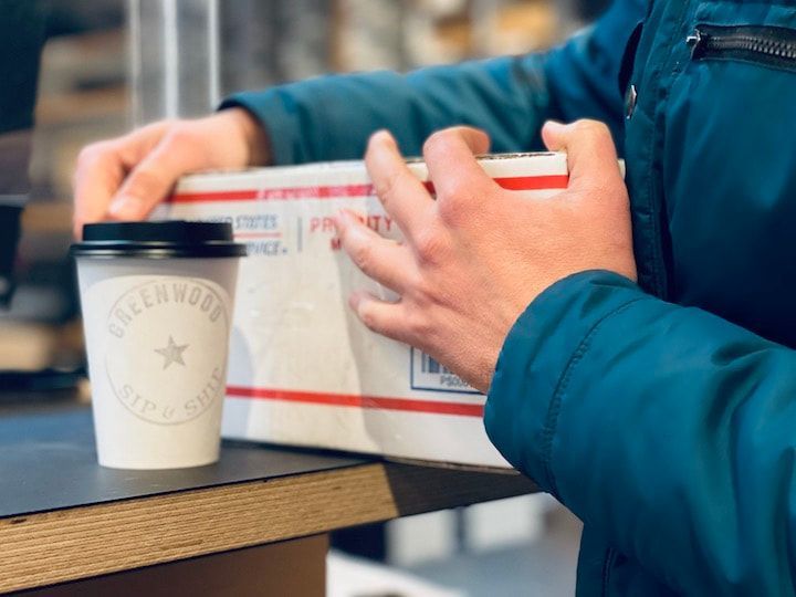 Hands holding a white-and-red food box beside a takeaway coffee cup on a table