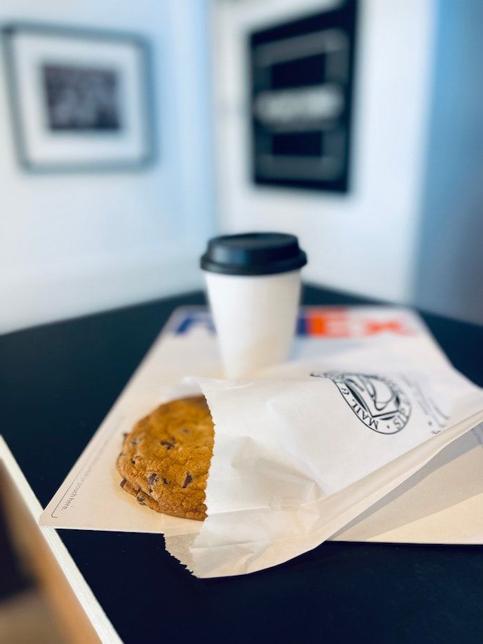 Coffee cup and cookie on a table in a café, with blurred wall art in the background.