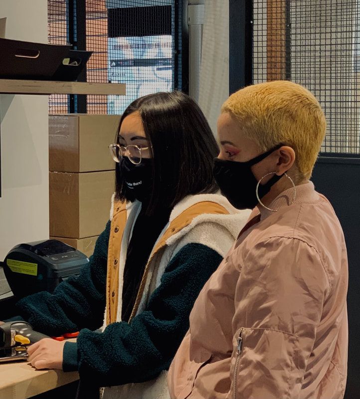 Two people wearing masks working at computers in an office-like setting.