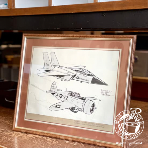 Framed black-and-white jet concept sketch in a brown frame on a wooden shelf.