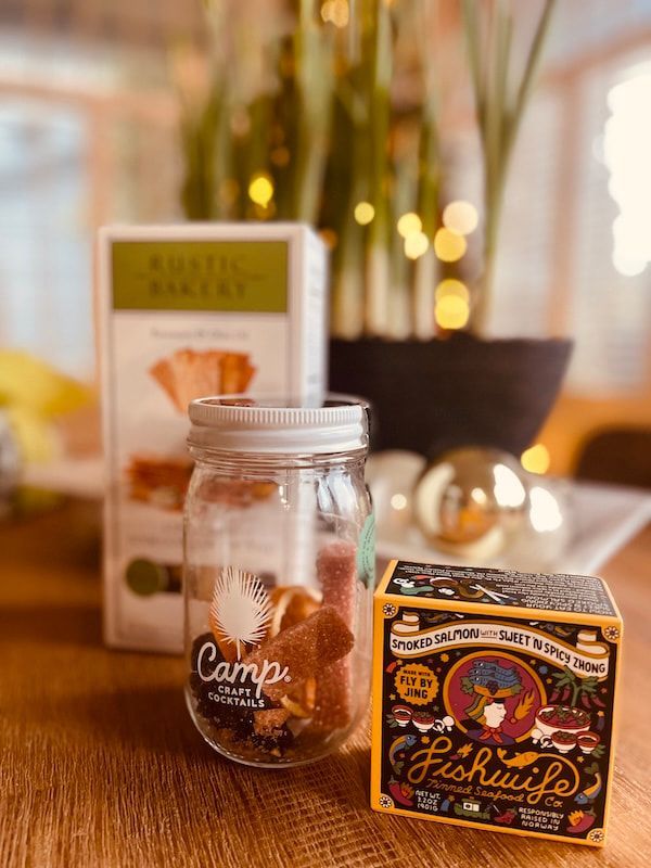 Glass jar of granola beside a colorful snack box on a warm, blurred tabletop display