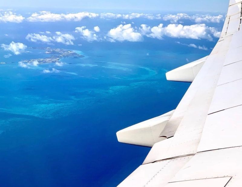 View from airplane window over blue ocean and clouds, with the wing in the foreground