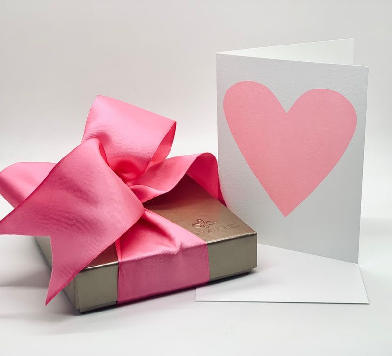 Pink ribbon-tied gift box beside a white card with a pink heart