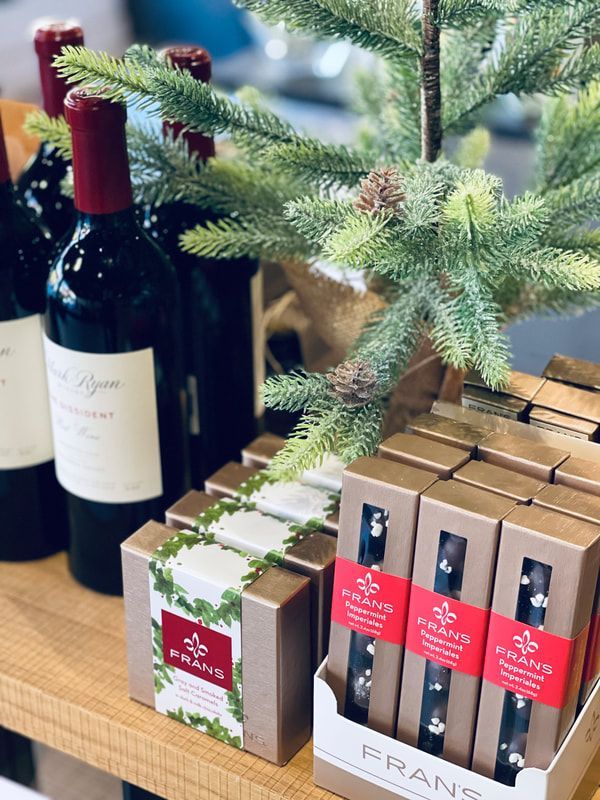 Holiday gift display with wine bottles, boxed chocolates, and evergreen branches on a wooden table