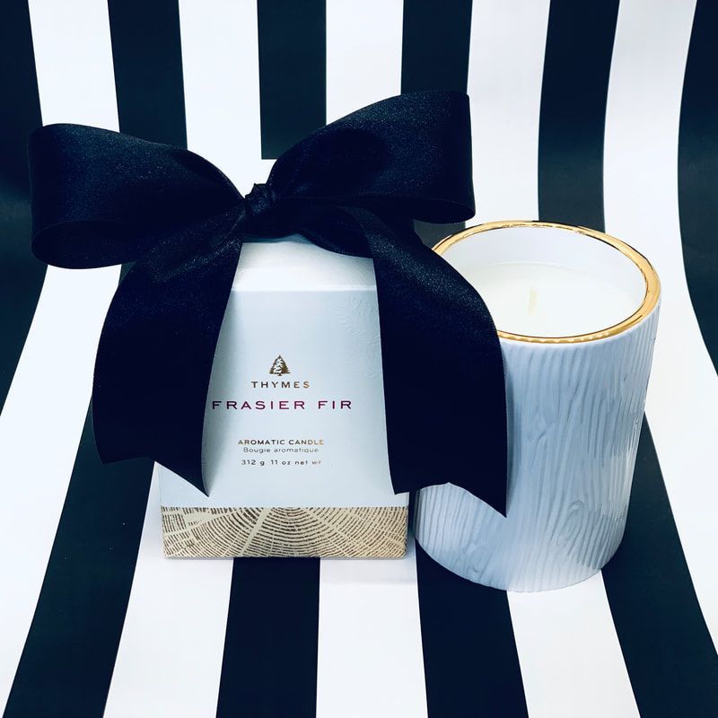 Gift box with a large black bow beside a white textured candle on black-and-white striped fabric.