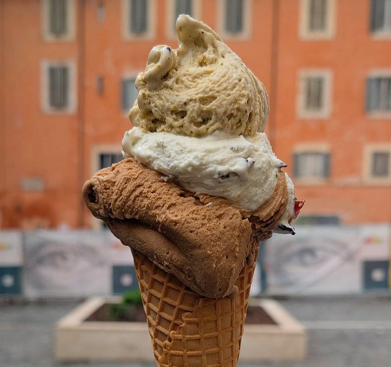 Three-scoop ice cream cone with tan, white, and brown flavors against an orange building background