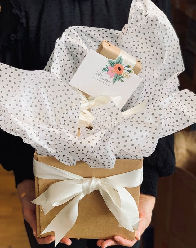 Gift basket wrapped in white polka-dot tissue with a cream ribbon and floral tag