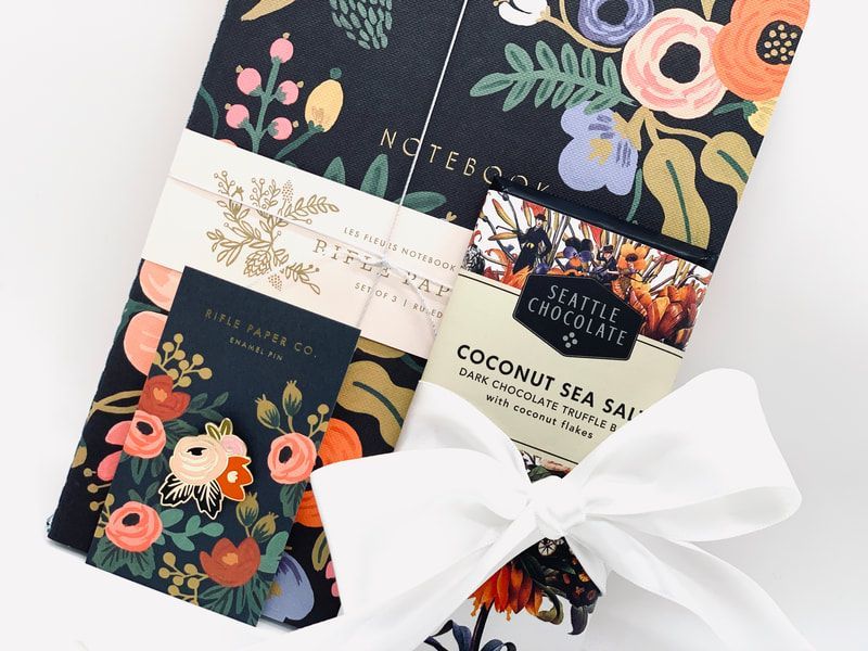 Gift set with floral-packaged soaps, a candle, and a white ribbon on a light background
