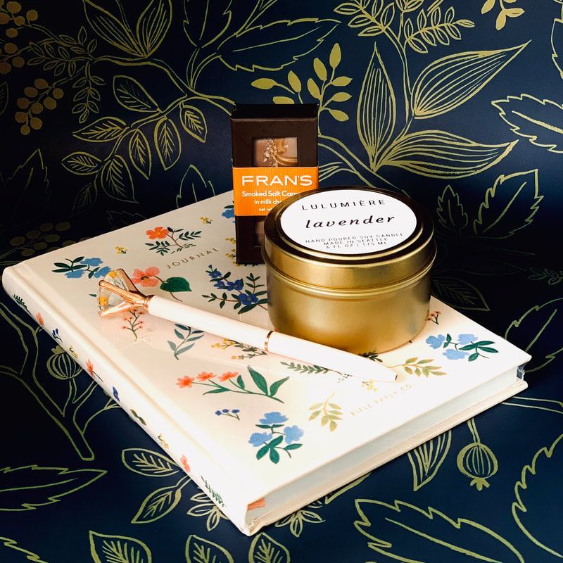 Floral gift set with a gold candle, tea box, and floral notebook on a dark botanical background