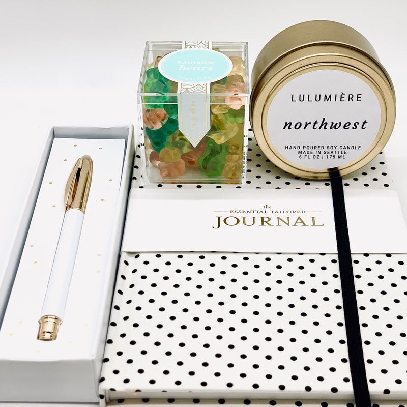 Journal, gold pen, polka-dot notebook, candle, and gift box arranged on a white surface.