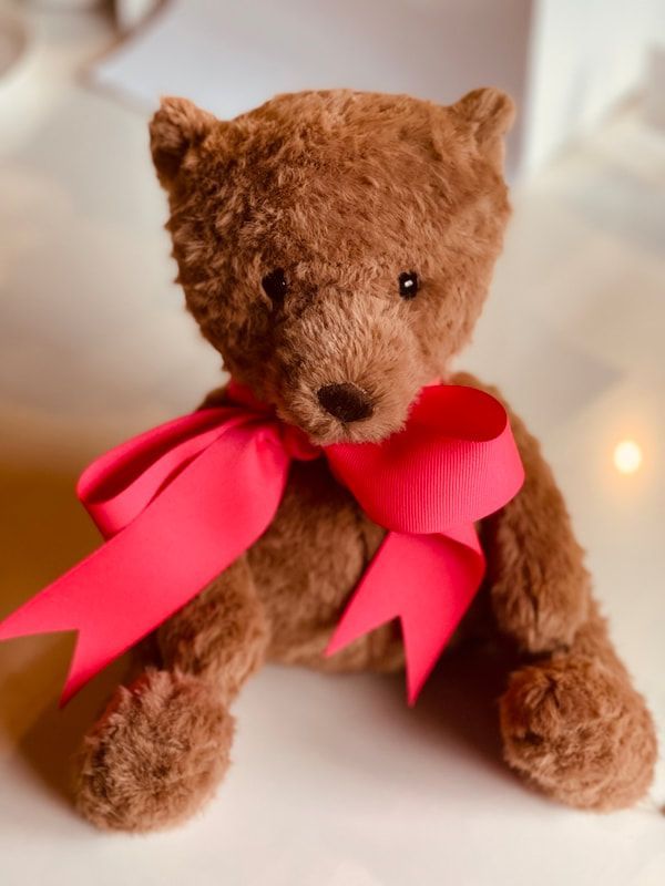 Brown teddy bear with a bright pink ribbon bow on a soft white background