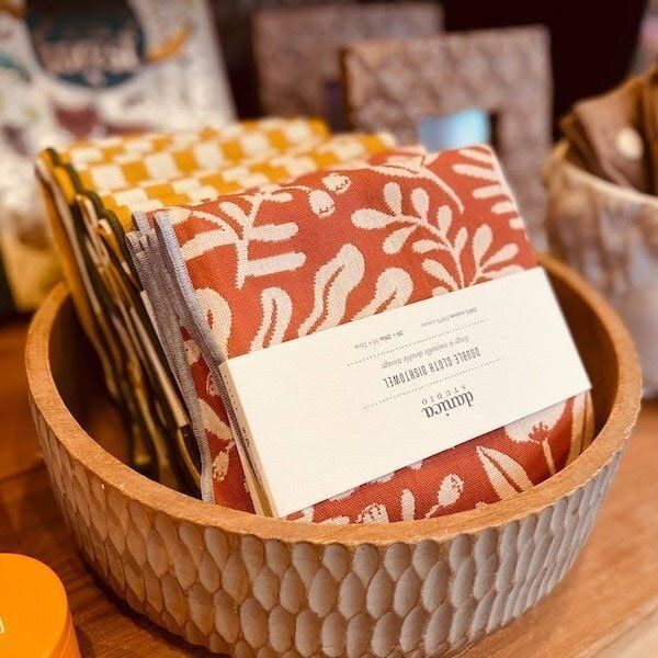 Patterned notebooks in a woven basket with a white label, displayed on a table.