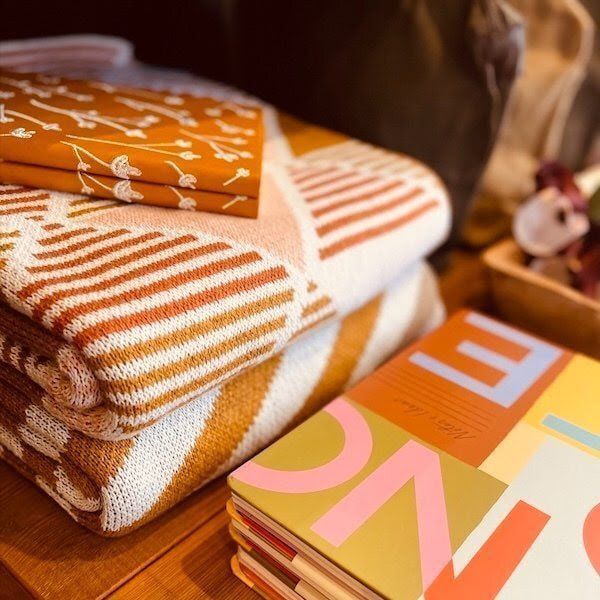 Folded orange and white blankets stacked beside a colorful notebook on a wooden surface