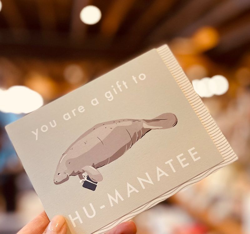 A hand holds a card reading “You are a gift to the sea” with a manatee illustration.