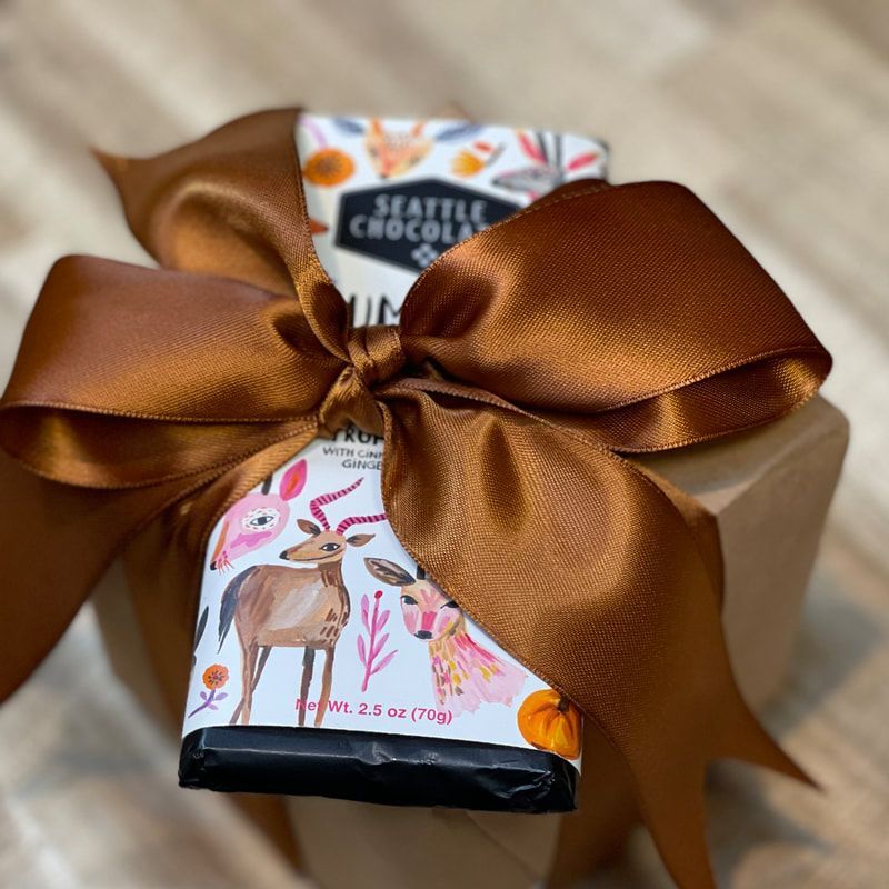 Gift box wrapped with a large brown satin bow and a Seattle Chocolate bar on top