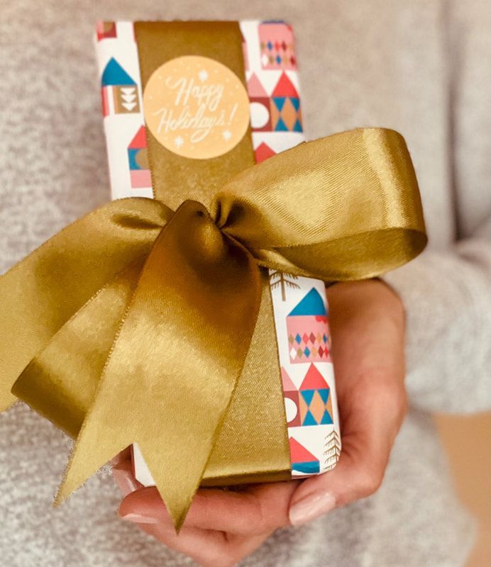 Wrapped gift with gold ribbon and patterned sides held in a person’s hands