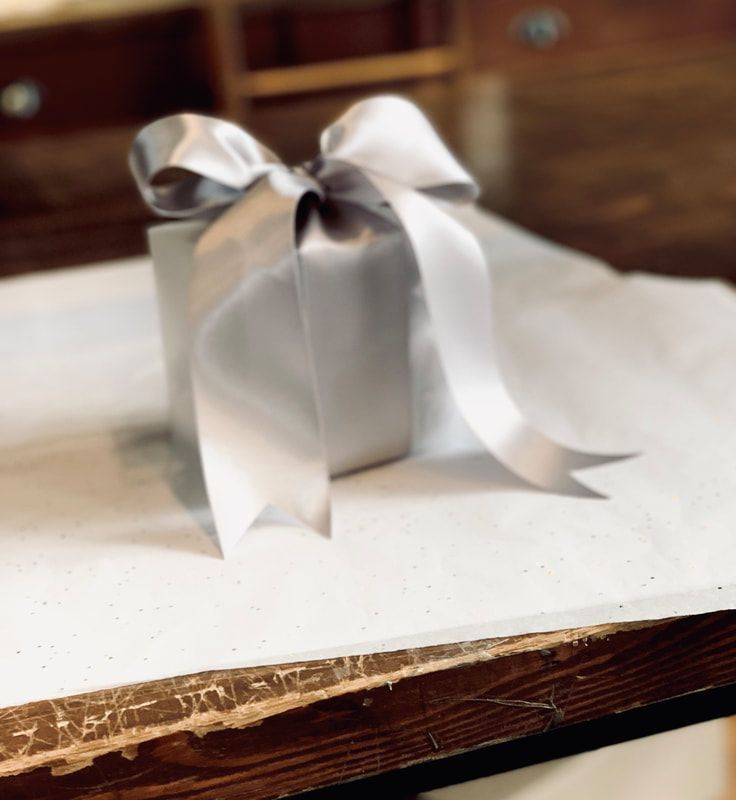 Small silver gift box with a white ribbon bow on a white tabletop.