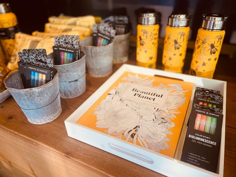 Assorted packaged candles and gift sets on a wooden table, including yellow tumblers and a white/orange box.