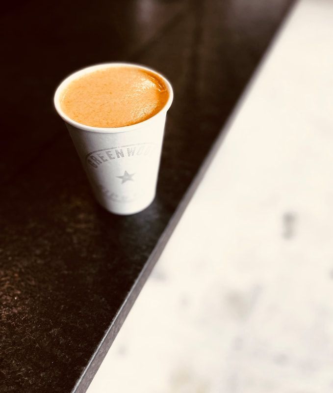 White cup of orange coffee on a dark table beside a light marble surface