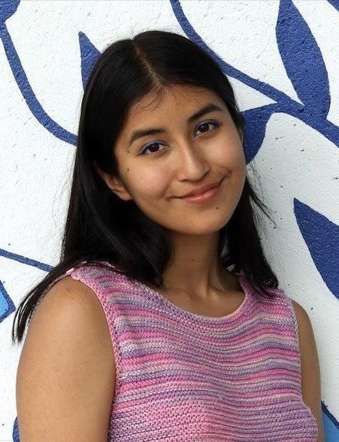 Smiling person in a pink sleeveless top standing against a white wall with blue mural lines