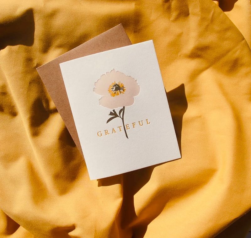 Thank-you card on golden fabric, featuring a white flower illustration and soft brown envelope